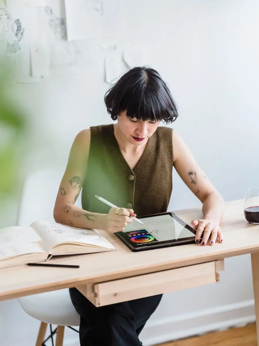 Designer with short dark hair drawing on a tablet at a wooden desk in a bright studio
