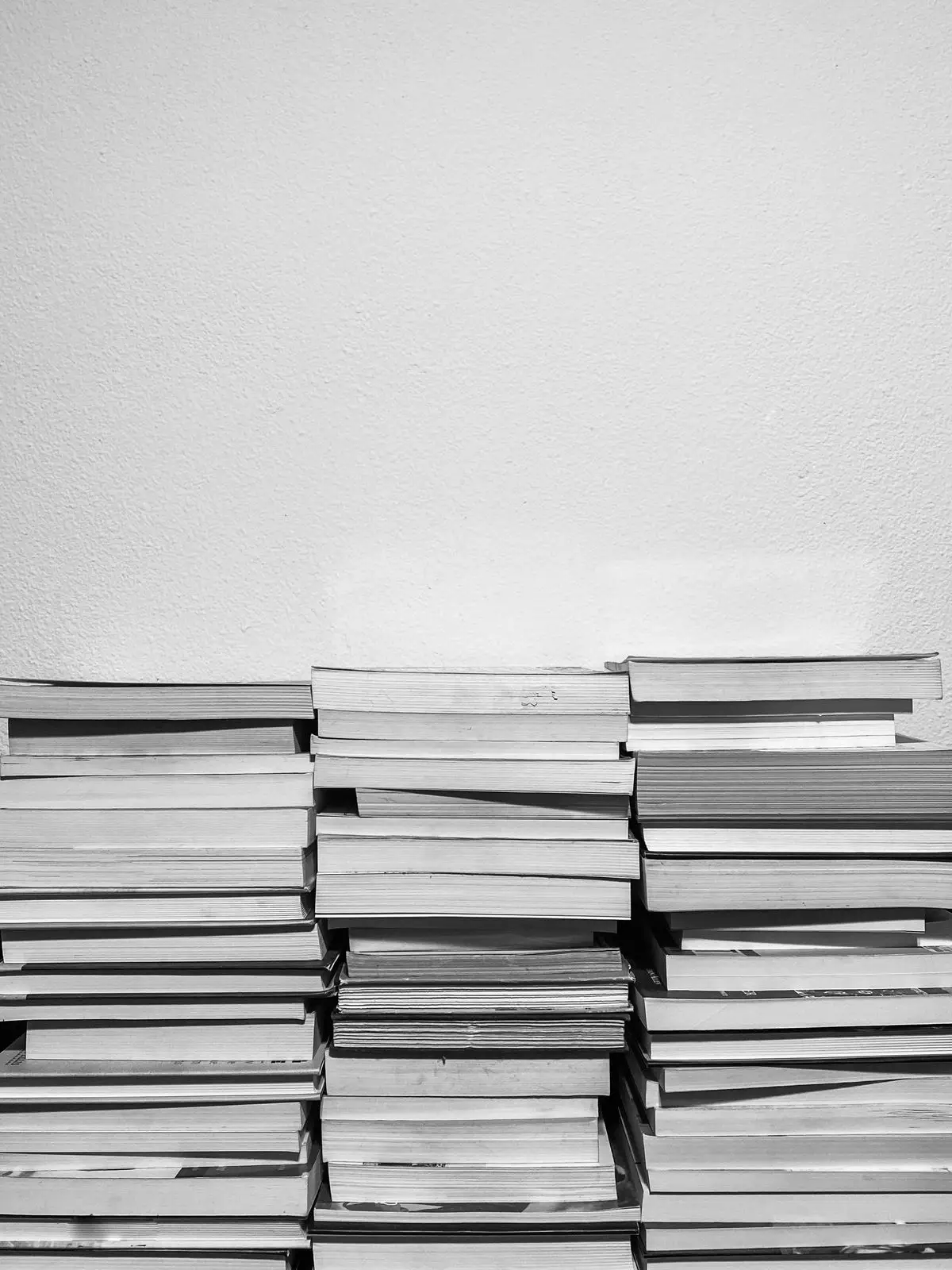 Stacks of paperback books piled against a white wall
