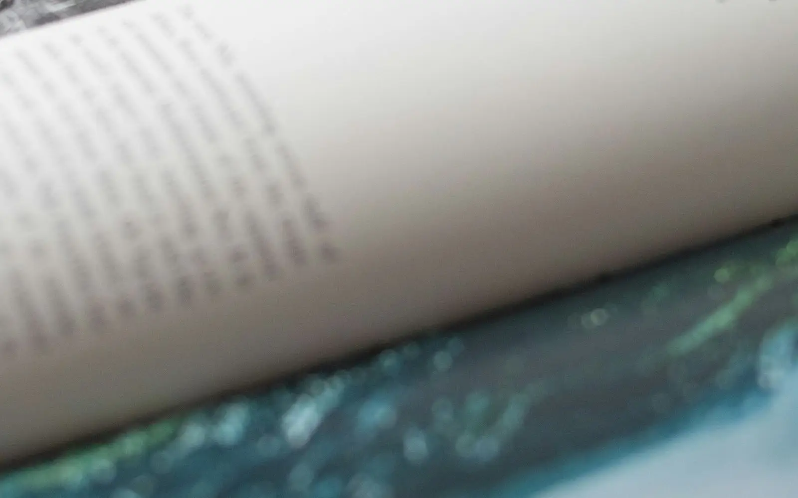 Close view of an open book, its text soft with shallow focus, over a blue-green cover