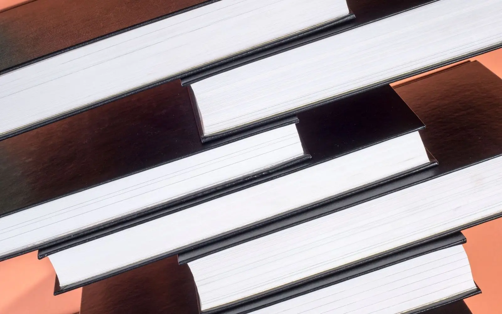 Black hardcover books stacked at angles against a coral wall