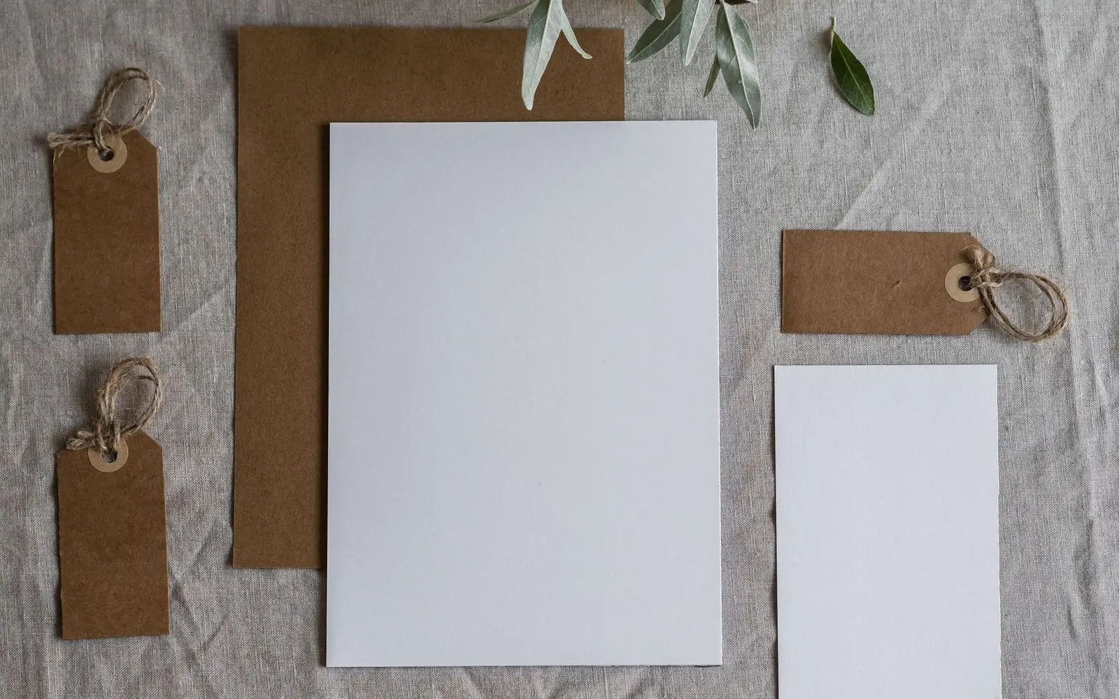 Blank letter sheets, kraft envelopes and tied paper tags laid out on linen