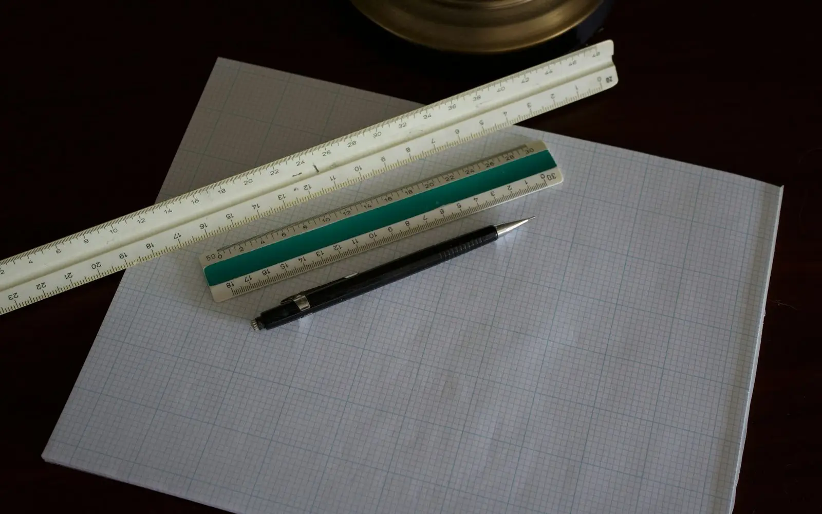 Two scale rules and a mechanical pencil lying on sheets of fine grid paper